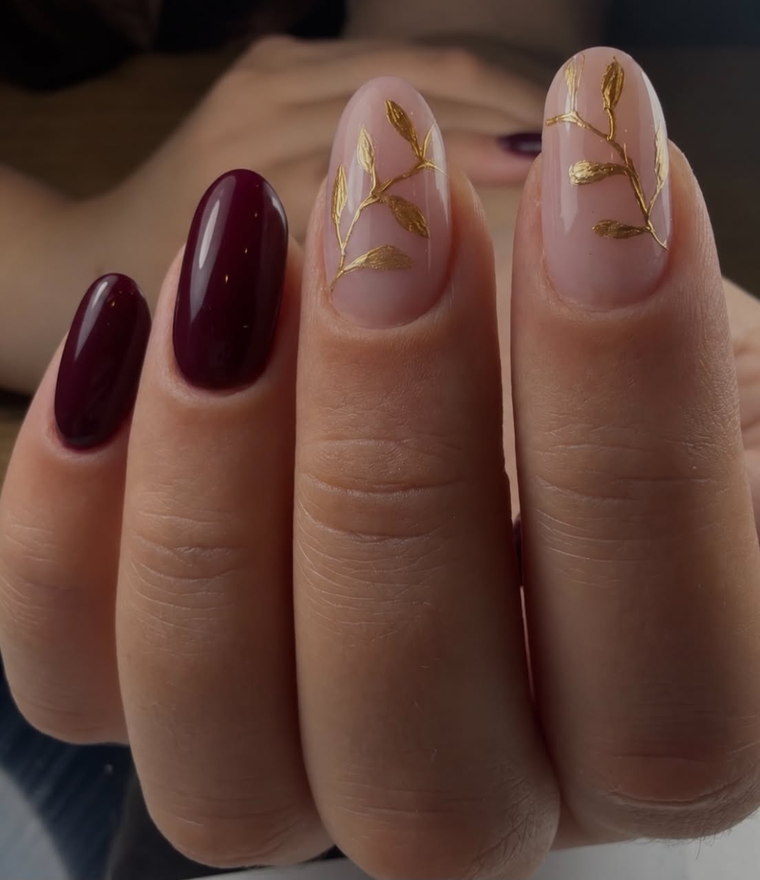 Nude nagels met bordeauxrode kleur en gouden takjes